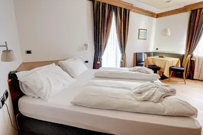 two beds in a hotel room with a table at Leading Relax Hotel Maria in Moena