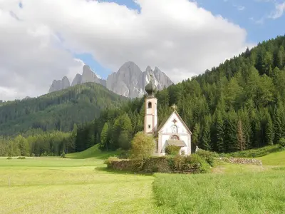 a small church in a field with mountains in the background at Haus Tannenburg in Funes