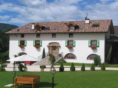 a large white house with green shuttered windows at Maso Chelò in Cavalese