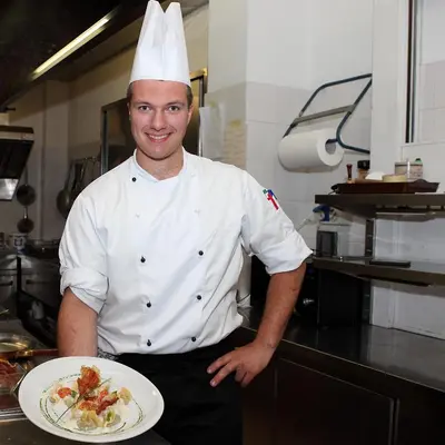 a chef holding a plate of food in a kitchen at Park Hotel Arnica in Falcade