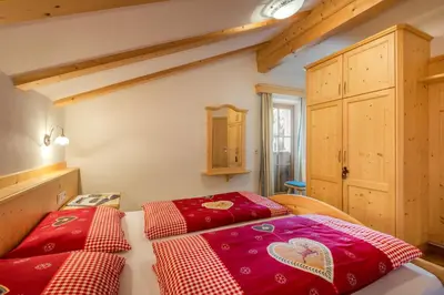 two beds in a room with red sheets at Appartamenti Maierhof in La Valle