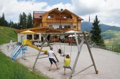 three children playing on a playground in front of a house at Rifugio La Para in San Vigilio Di Marebbe