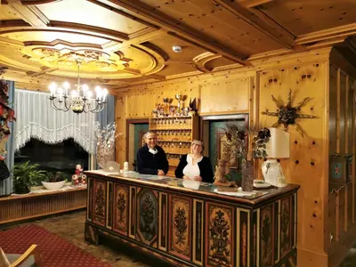 two women standing behind a counter in a room with a fireplace at Hotel la Plaza in Corvara in Badia