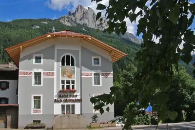 a large white building with a mountain in the background at Hotel San Giovanni in Vigo di Fassa