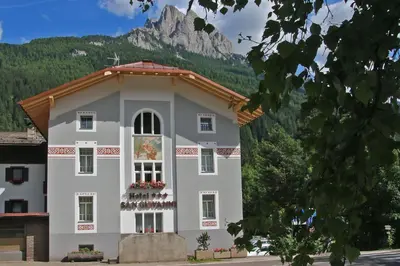 a large white building with a mountain in the background at Hotel San Giovanni in Vigo di Fassa