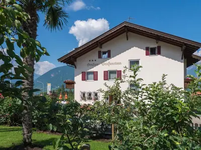 a white house with mountains in the background at Guesthouse Pension Grafenstein in Merano
