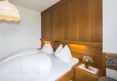 a bedroom with a white bed with a wooden headboard at Guesthouse Pension Grafenstein in Merano