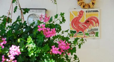 a picture of a rooster on a wall with pink flowers at Stocknerhof in Bressanone