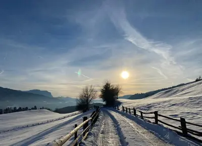 a snow covered field with a fence and the sun at Stocknerhof in Bressanone