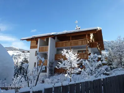 a house covered in snow in front of a fence at Ciasa Isidor in San Vigilio Di Marebbe