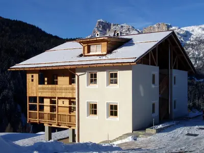 a house in the snow with mountains in the background at Apartments Serghela in San Cassiano