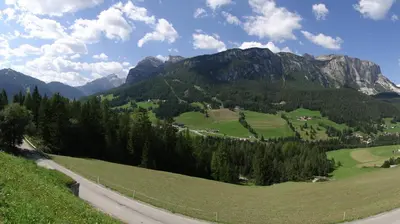 a road in the mountains with a green field and trees at Appartamenti Suttru in Badia