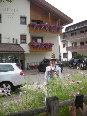 a man standing in a field of flowers in front of a building at Garni Hotel Rezia in Selva di Val Gardena
