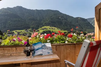 a table with a bottle of wine and a book on a balcony with flowers at AppartChalet LA RONDULA - 100m from Seceda in Ortisei