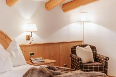 a bedroom with a bed and a chair and lamp at B&B Hotel Mirabel in Ortisei