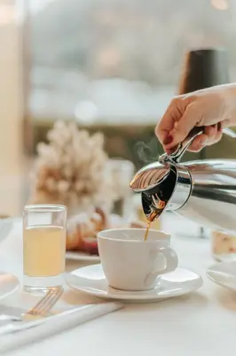 a person pouring coffee into a cup on a table at B&B Hotel Mirabel in Ortisei