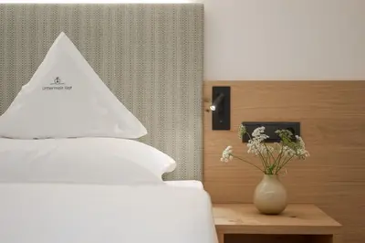 a white bed with a white pillow and a vase with flowers at Untermairhof in Lagundo