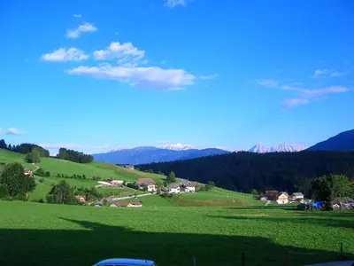 a green field with houses and mountains in the background at Hotel Dolomitenblick in Terento