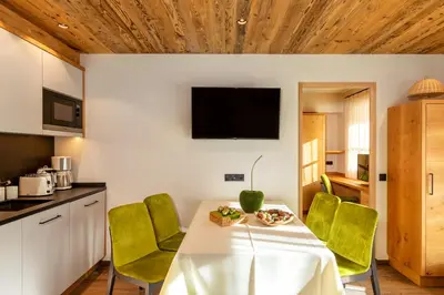 a kitchen and dining room with a white table and green chairs at Chalets 4 Sorus & Apartments La Villetta in Colfosco