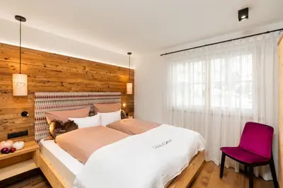 a bedroom with a large bed and a red chair at Chalets 4 Sorus & Apartments La Villetta in Colfosco