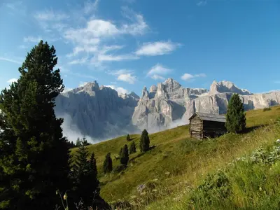 an old barn on a hill with mountains in the background at Residence Bondì in Colfosco