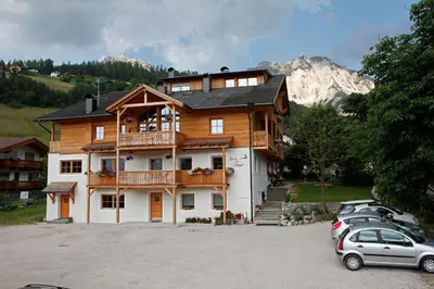 a large house with cars parked in a parking lot at Garnì Iosc in San Vigilio Di Marebbe