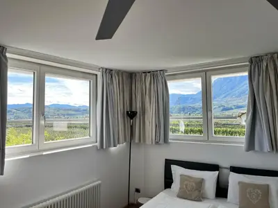 a bedroom with a bed and three windows with mountains at B&B Mele d'Oro in Bolzano