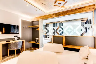 a room with a bed and a desk and a window at Hotel Muliac in Selva di Val Gardena