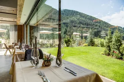 a dining room with a table with a view of a garden at Hotel Muliac in Selva di Val Gardena