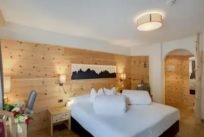 a large white bed in a room with wooden walls at Hotel Muliac in Selva di Val Gardena