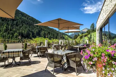 a patio with tables and chairs with mountains in the background at Hotel Muliac in Selva di Val Gardena