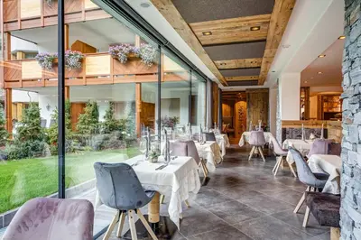 a restaurant with white tables and chairs and large windows at Hotel Muliac in Selva di Val Gardena