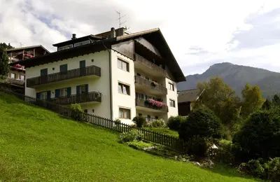 a large white building on a hill with a green field at Appartements Arnica in Ortisei