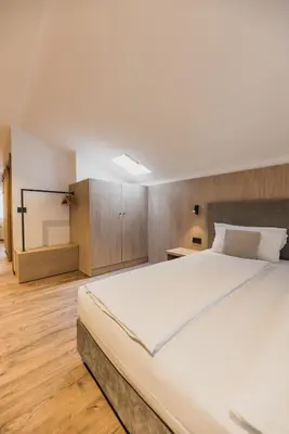 a bedroom with a large white bed and wooden floors at Suàn Hotel in Ziano di Fiemme