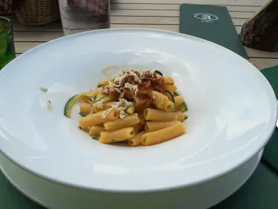 a white plate of pasta with a pickle at Chalet Prà delle Nasse in San Martino di Castrozza