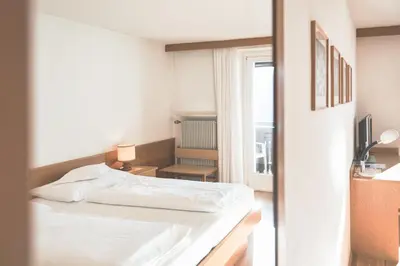 a white bedroom with a bed and a window at Hotel Gasthof Stern in Nova Ponente