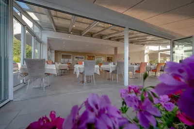 a dining room with white tables and chairs and purple flowers at Garni Hotel Peterlinhof in Caldaro