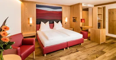 a bedroom with a bed and a red chair at Hotel Hasslhof in Caldaro