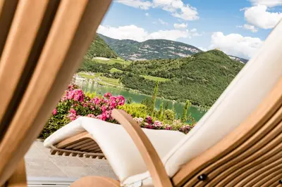 a chair with a view of a lake and mountains at Hotel Hasslhof in Caldaro