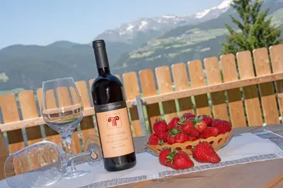 a bottle of wine and a bowl of strawberries on a table at Forchnerhof Panorama- Rienzschlucht in Rodengo