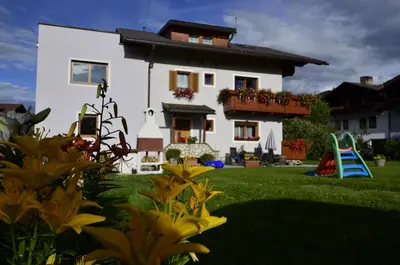 a white house with a yard with flowers and a playground at Haus Cosso in Villabassa