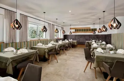a dining room with tables and chairs and windows at Appartement-Hotel Anthea in Tirolo