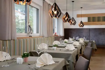 a restaurant with gray tables and chairs and chandeliers at Appartement-Hotel Anthea in Tirolo
