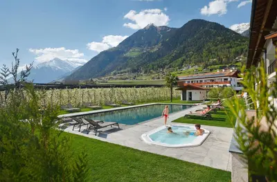 two people in a swimming pool with mountains in the background at Appartement-Hotel Anthea in Tirolo