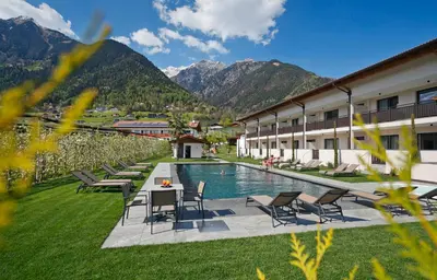 a hotel with a pool and chairs and mountains at Appartement-Hotel Anthea in Tirolo