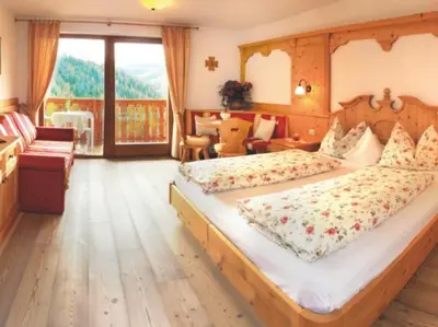 a bedroom with a large bed and a balcony at Hotel Alpenrose Dolomites in La Valle