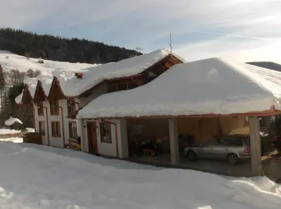 a house covered in snow with a car parked in front at B&B Affittacamere Larix in Rumo