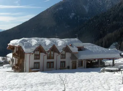 a house covered in snow with mountains in the background at B&B Affittacamere Larix in Rumo