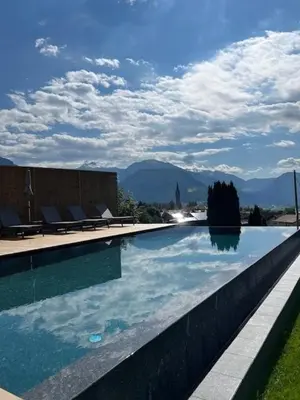 a swimming pool with chairs and mountains in the background at Hotel Lahnerhof in Vipiteno