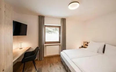 a bedroom with a bed and a desk and a window at Hotel Lahnerhof in Vipiteno